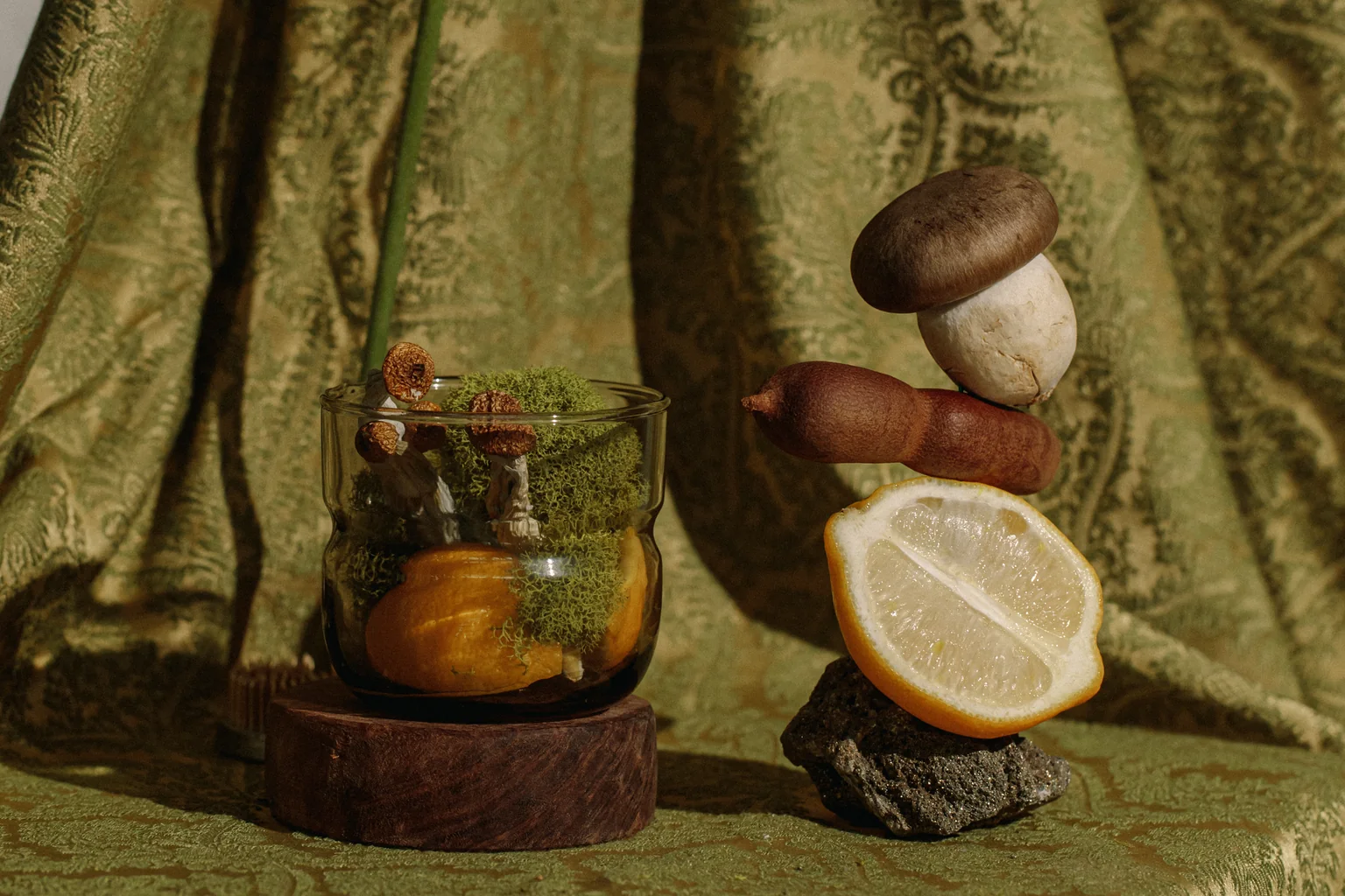 Fresh mushrooms, a lemon and a glass on draped green fabric.