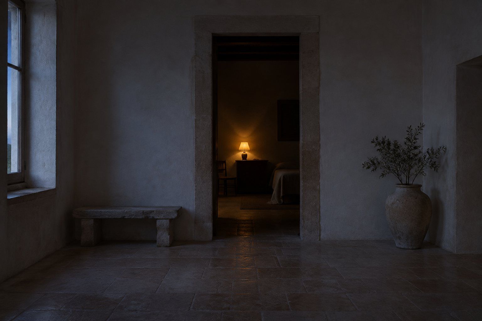 A pale stone room at dusk, with a narrow doorway and a warm lamp in the room beyond.